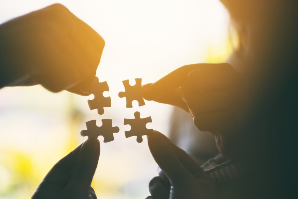 Silhouette image of many people holding and putting a piece of white jigsaw puzzle together